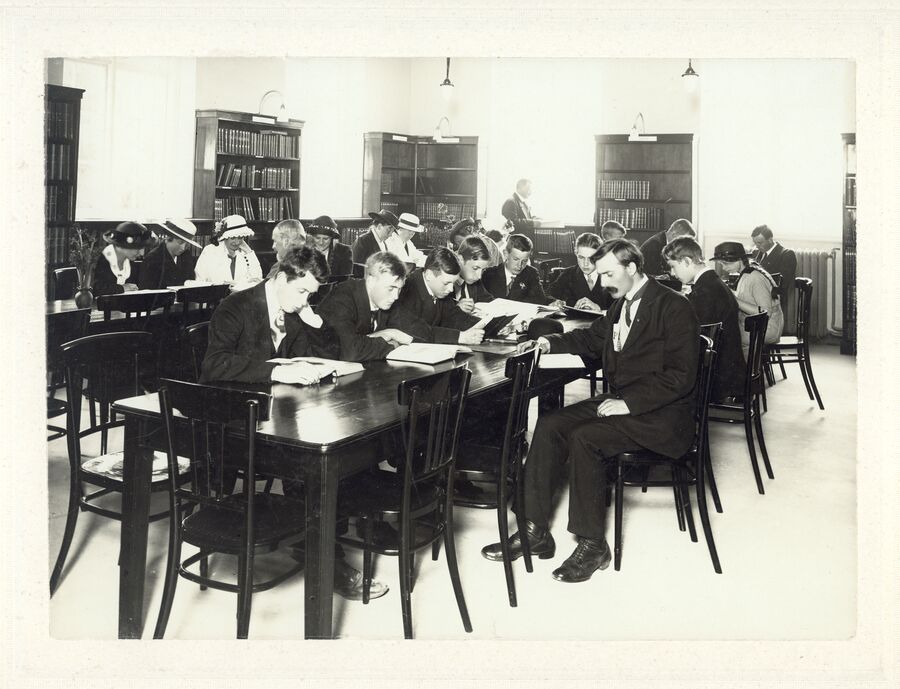 Mennesker i 1915 sitter rundt et bord og leser